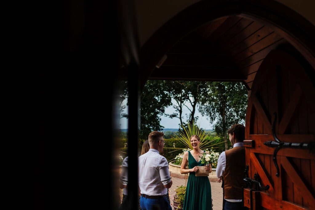 Elegant outdoor wedding ceremony with bridesmaids and groomsmen, captured through rustic wooden gate, highlighting wedding celebration and joyful moments in natural setting, perfect for wedding photography SEO.