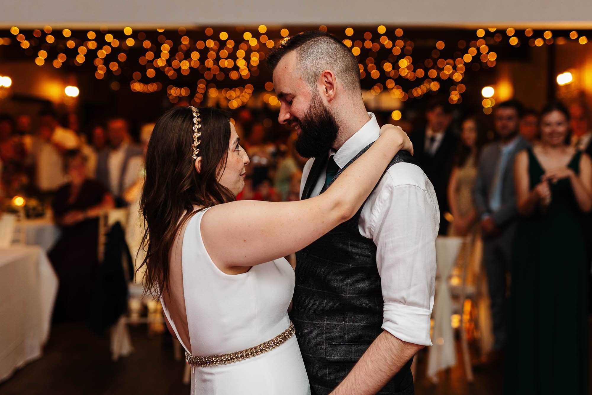 Goosedale wedding photographer Elegant bride and groom sharing first dance at a wedding reception, with warm ambient lighting in the background.