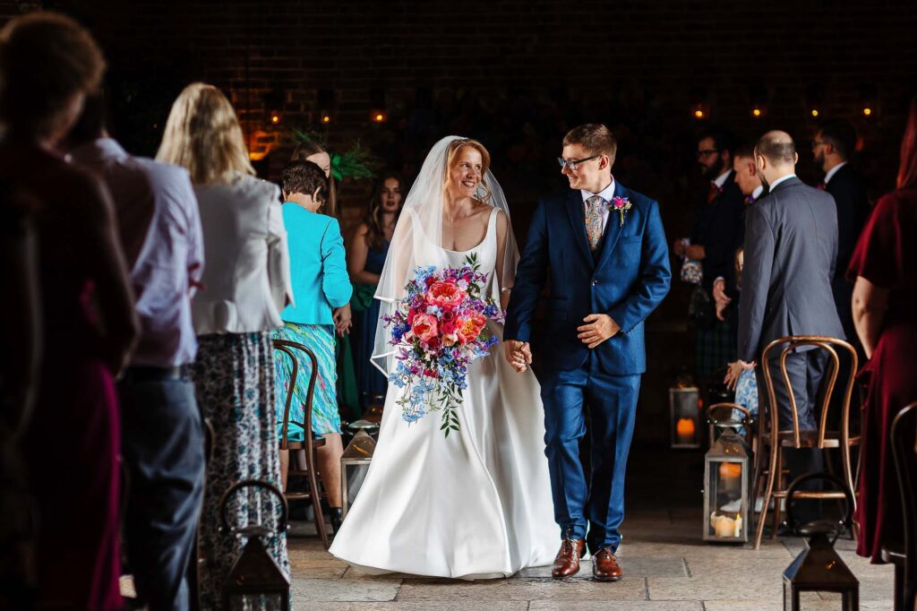 Vibrant wedding ceremony at BGS Weddings, featuring a bride and groom sharing a joyful moment with guests in a stylish indoor setup with lanterns and warm lighting.