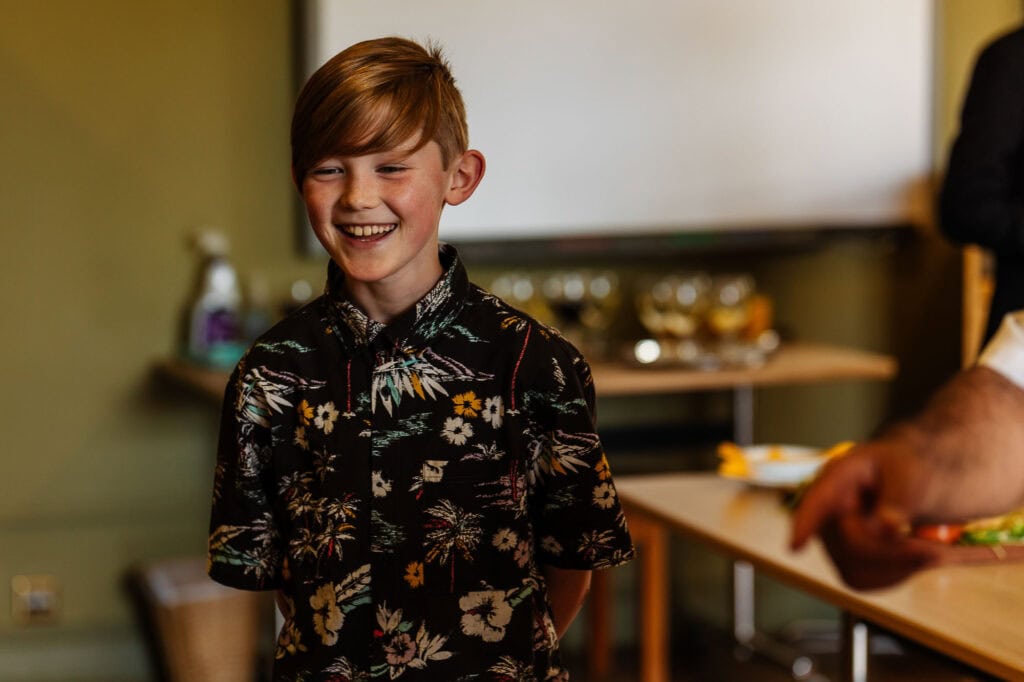 Joyful young boy smiling at a wedding reception, wearing a colourful floral shirt, engaged in celebratory moments, captured in a candid, vibrant atmosphere—ideal for wedding event photography and family celebration visuals.