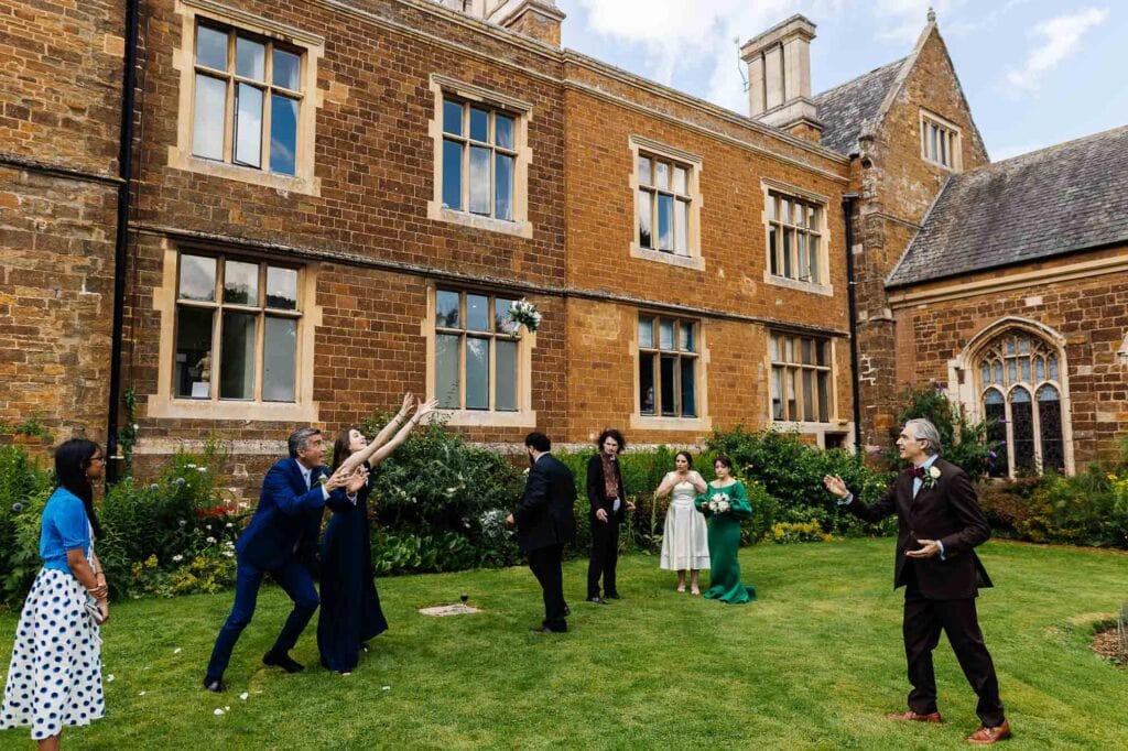 Celebrating a wedding outside a historic stone church with joyful guests throwing confetti and enjoying the beautiful garden setting, capturing a memorable wedding moment.