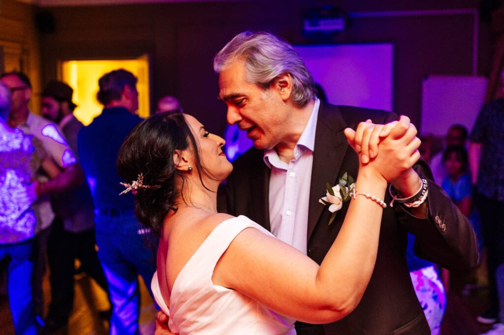 Elegant couple dancing at wedding reception, capturing romantic moment with colorful lighting and joyful guests in the background.