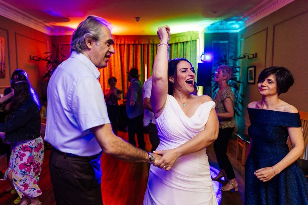 Elegant bride enjoying her wedding reception with joyful dance in a colourful, lively venue, celebrating love and happiness surrounded by family and friends at BGS Weddings.