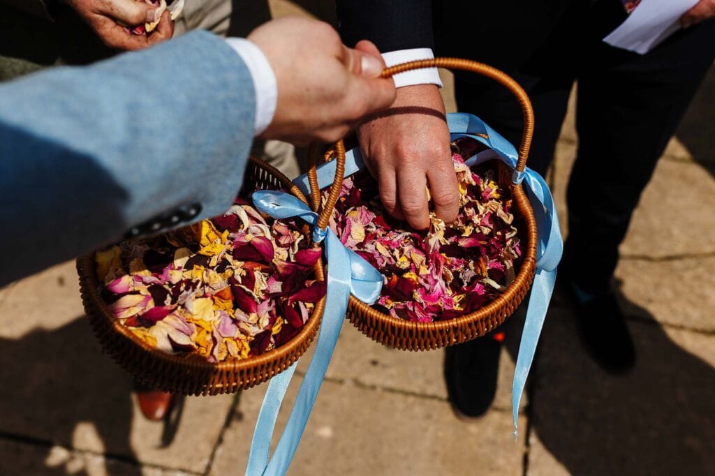 Petal exchange at a wedding, close-up of hands holding a basket of colourful flower petals, traditional wedding ceremony, outdoor setting, romantic atmosphere, BGS Weddings for memorable wedding moments.
