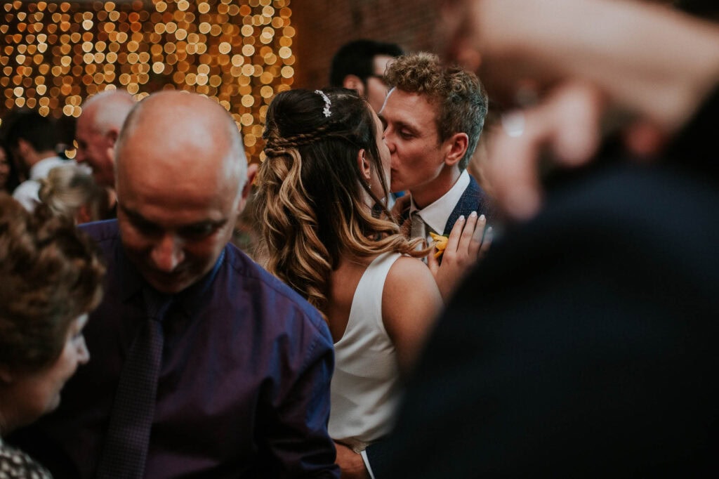 Romantic wedding couple sharing a kiss at a beautifully decorated reception, capturing a heartfelt moment in a joyful celebration, with warm lighting and elegant attire.