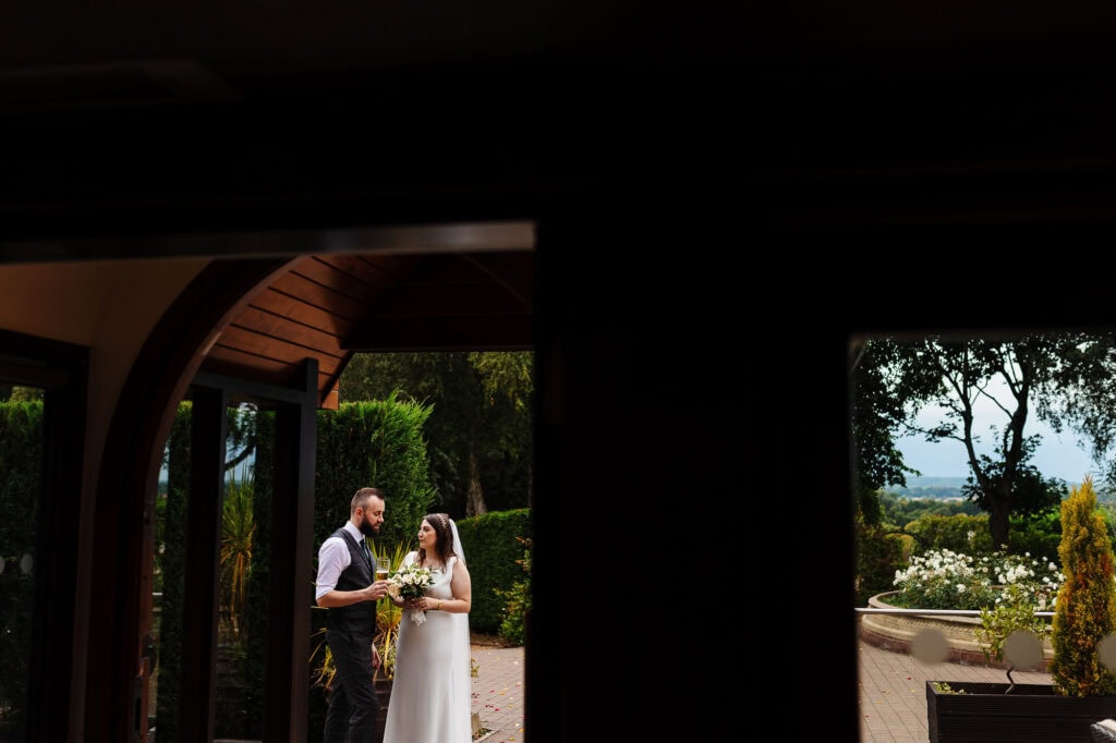 Elegant bride and groom sharing a toast outdoors at their wedding reception, surrounded by lush greenery and scenic landscape, captured by BGS Weddings for a memorable special day.