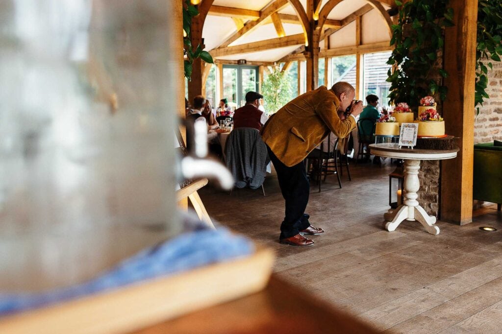 Elegant wedding photographer capturing guests at a rustic wedding venue with wooden beams and floral decorations.