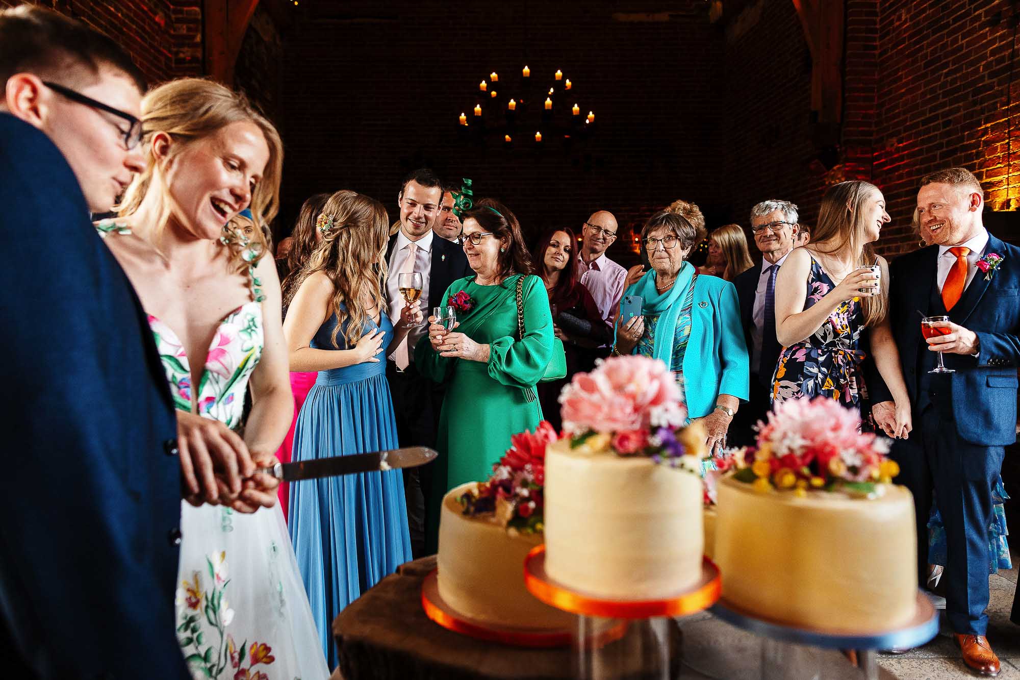 Elegant wedding celebration with guests around a beautifully decorated wedding cake at BGS Weddings in a rustic brick venue.