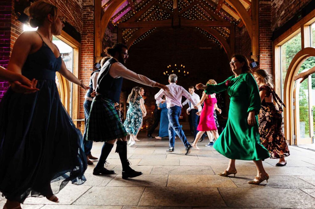 Vibrant wedding guests dancing at a rustic barn reception venue, showcasing joyful celebration and lively dancefloor atmosphere, ideal for wedding photography and event planning.