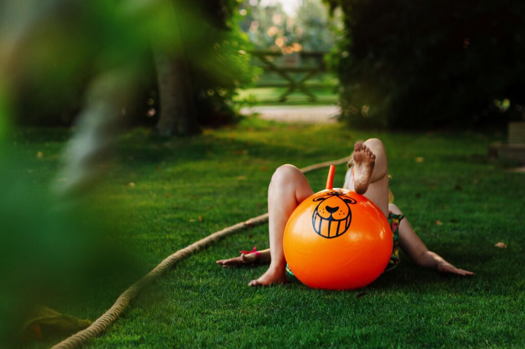 Inflatable orange lion ball on grass with child playing outdoors at garden party or event, fun and colourful summer activity, BGS Weddings UK photography.