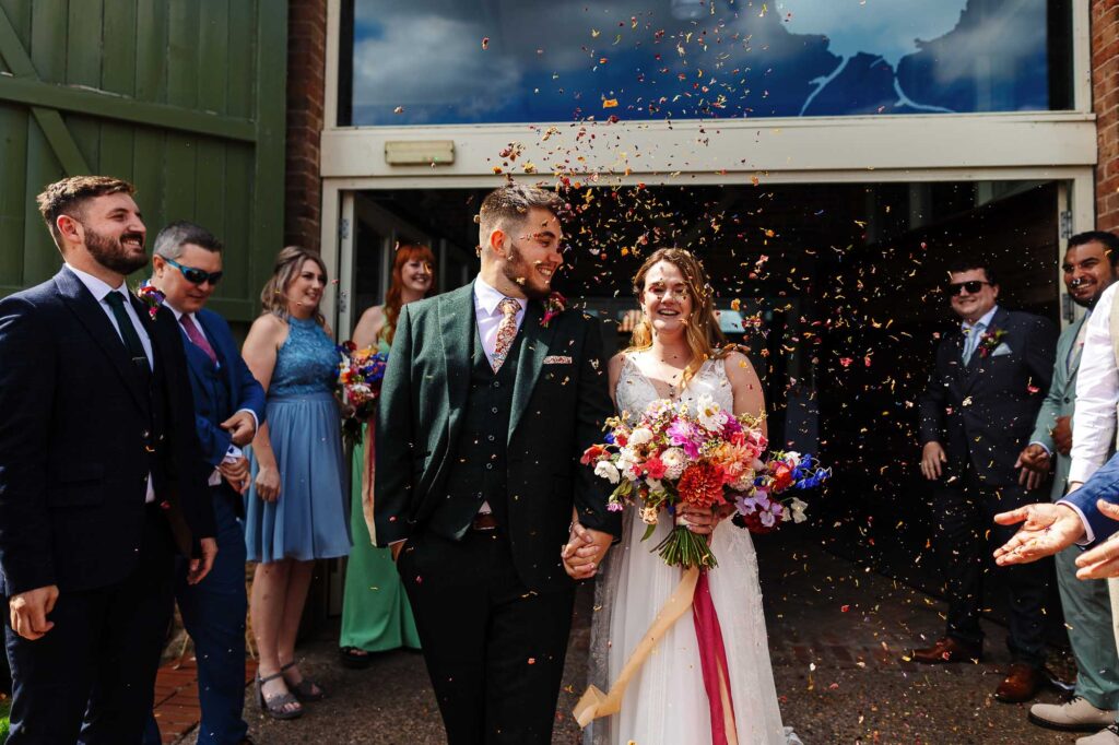 Celebrating a wedding at BGS Weddings with joyful newlyweds and guests, colourful confetti, and a beautiful outdoor venue in the UK.