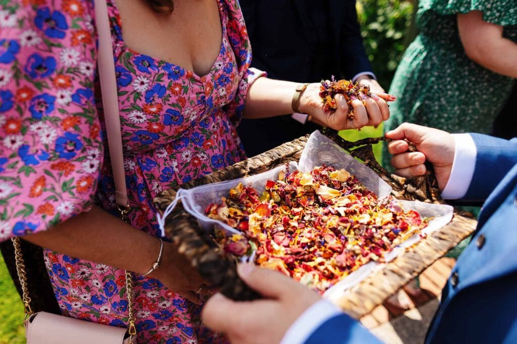 Bright floral wedding dress with colourful flower petals and hand-held basket during outdoor wedding ceremony.