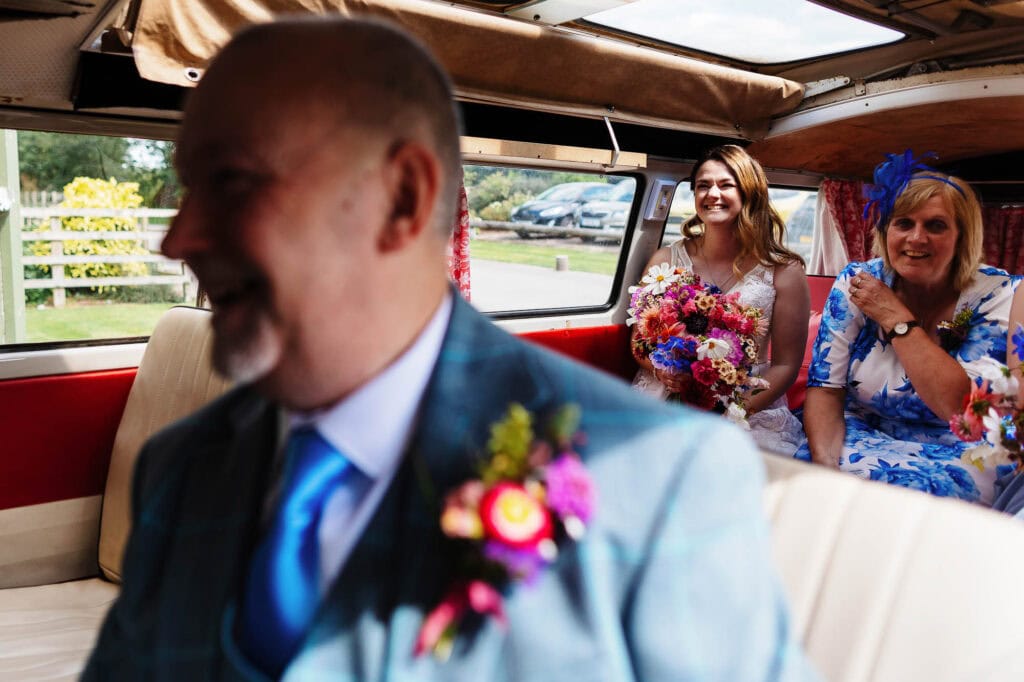 Vow renewal wedding celebration inside a vintage camper van with joyful family and bride holding a colourful bouquet.