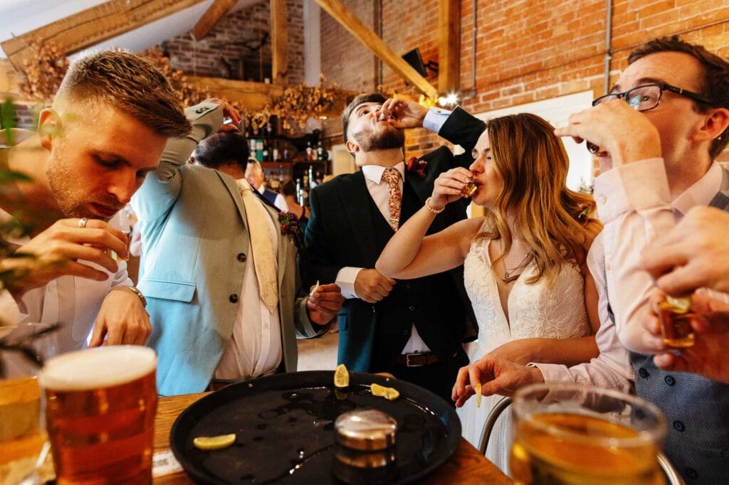 Relaxed wedding celebration at a rustic barn venue with friends enjoying drinks and shots, capturing joyful moments during the wedding reception.