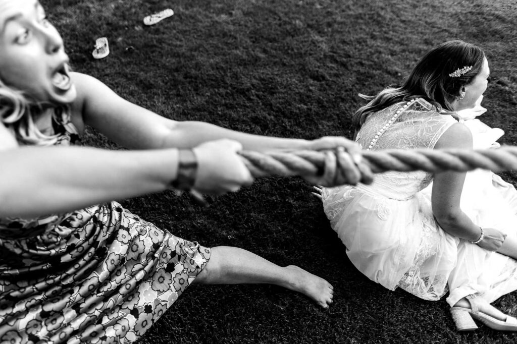 Aerial shot of a woman in a wedding dress being pulled on a rope during a wedding game at an outdoor celebration. Fun, playful wedding activities captured in black and white.