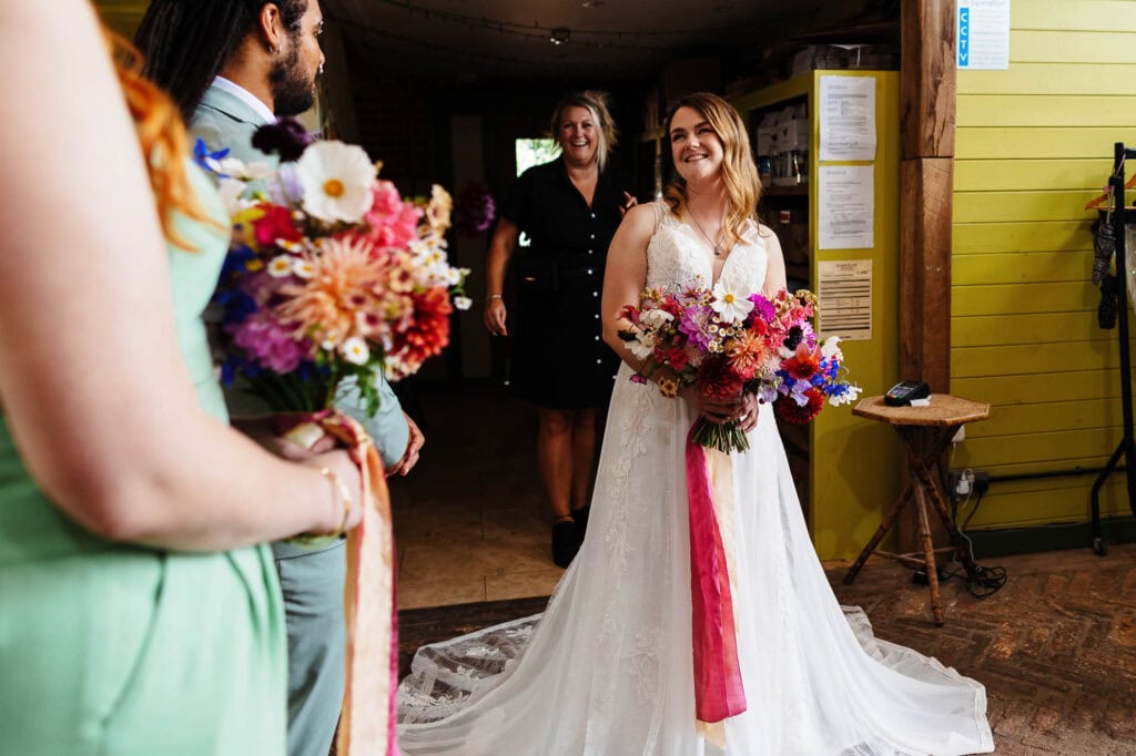 Vibrant bridal bouquet with colourful flowers, bride smiling inside a rustic venue, wedding day celebration, floral arrangement, joyful atmosphere at BGS Weddings, UK wedding photography.
