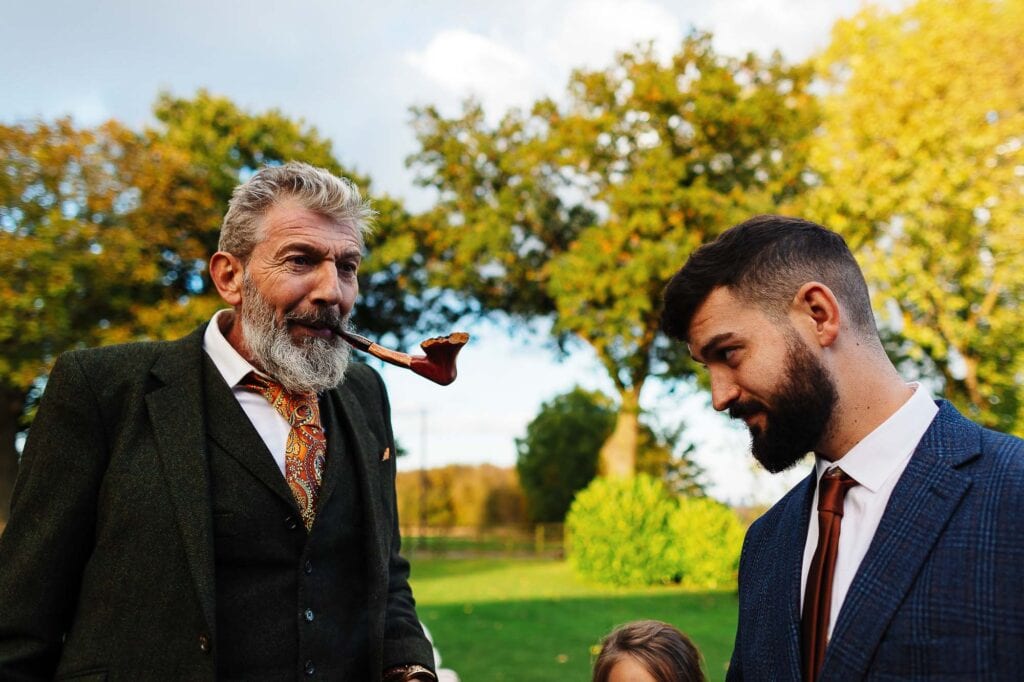 Elegant senior man with a pipe and smart young man in the garden during autumn, celebrating a special occasion with friends or family in a beautiful outdoor setting.