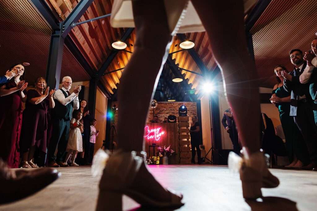 Elegant wedding dance at BGS Weddings with guests applauding and a romantic neon sign in a rustic indoor venue.