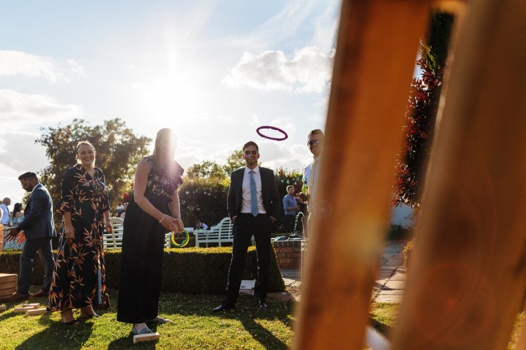 Outdoor garden wedding celebration with guests playing ring toss game, vibrant sunlight, and joyful atmosphere at BGS Weddings, offering professional wedding planning and event services in the UK.