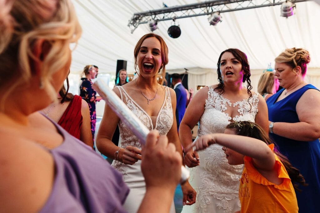 Festive wedding celebration with bridesmaids and guests dancing at a BGS Weddings event in a large, elegant marquee. Joyful atmosphere, colorful attire, and lively interactions highlight wedding entertainment and guest joy.
