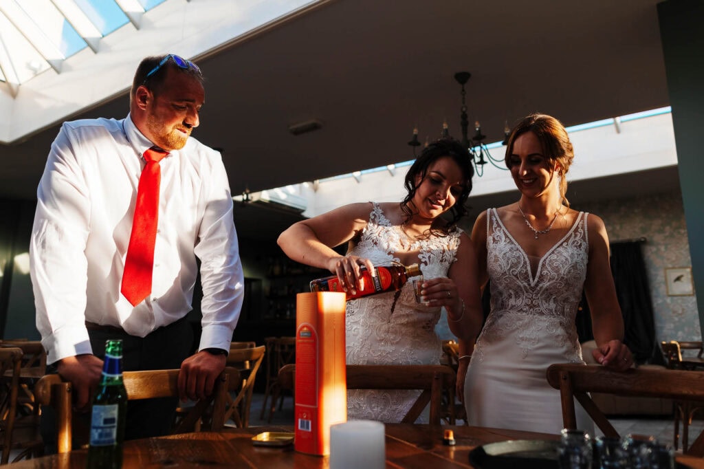 Elegant wedding celebration with bridesmaids, a groomsman, and a toast with whisky at BGS Weddings, capturing joyful moments, wedding attire, and festive atmosphere in an indoor venue.