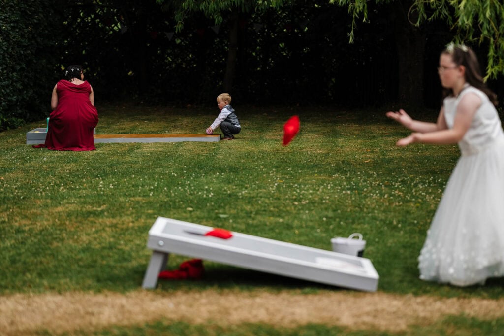 Throwing ring toss game at outdoor wedding reception with children and guests on lush green lawn, capturing fun and joyful moments.