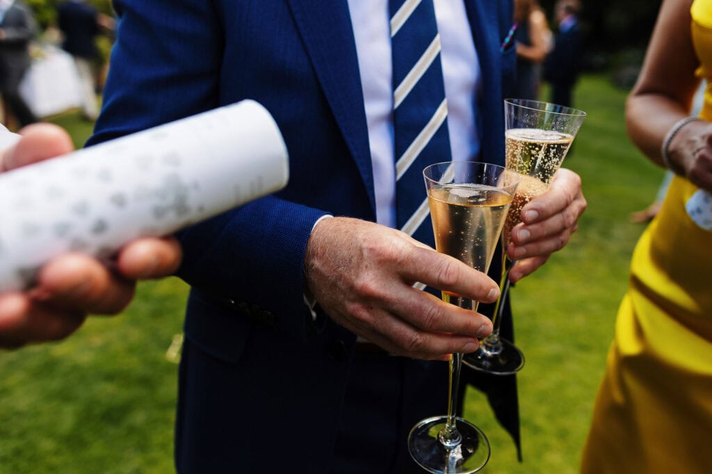 Cheers at outdoor wedding celebration, people holding champagne flutes, wedding toast, stylish attire, romantic event, wedding reception, celebrating love, garden wedding, bubbles on drinks, joyful atmosphere.