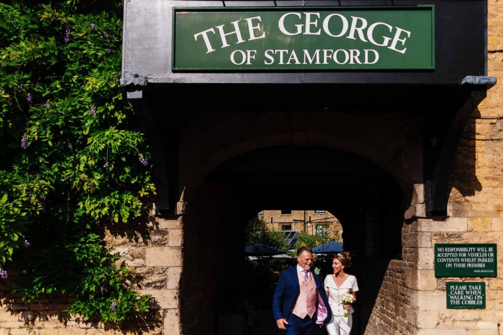 Elegant wedding couple walking through historic gate at The George of Stamford, featuring picturesque brick and lush greenery, perfect for wedding photography and elegant wedding venues.