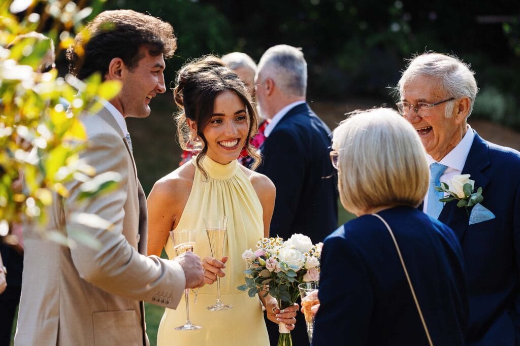 Elegant wedding reception, outdoor celebration with guests in formal attire, lady with bouquet and champagne, joyful moments, BGS Weddings photography focus.