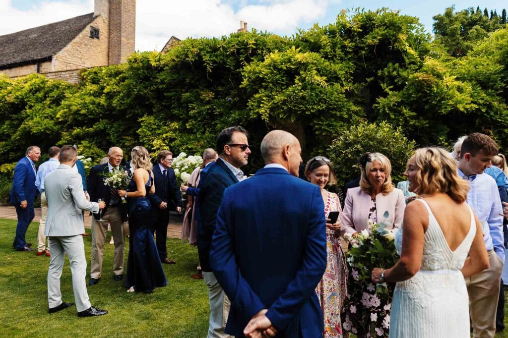 Elegant outdoor wedding gathering at BGS Weddings, featuring guests mingling on lush green lawns with beautiful floral arrangements and historic buildings in the background.