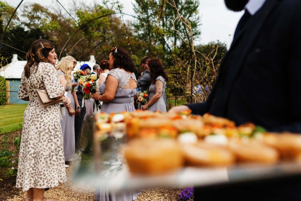 Elegant outdoor wedding reception with guests holding bouquets, celebrating amidst garden scenery at BGS Weddings in the UK.