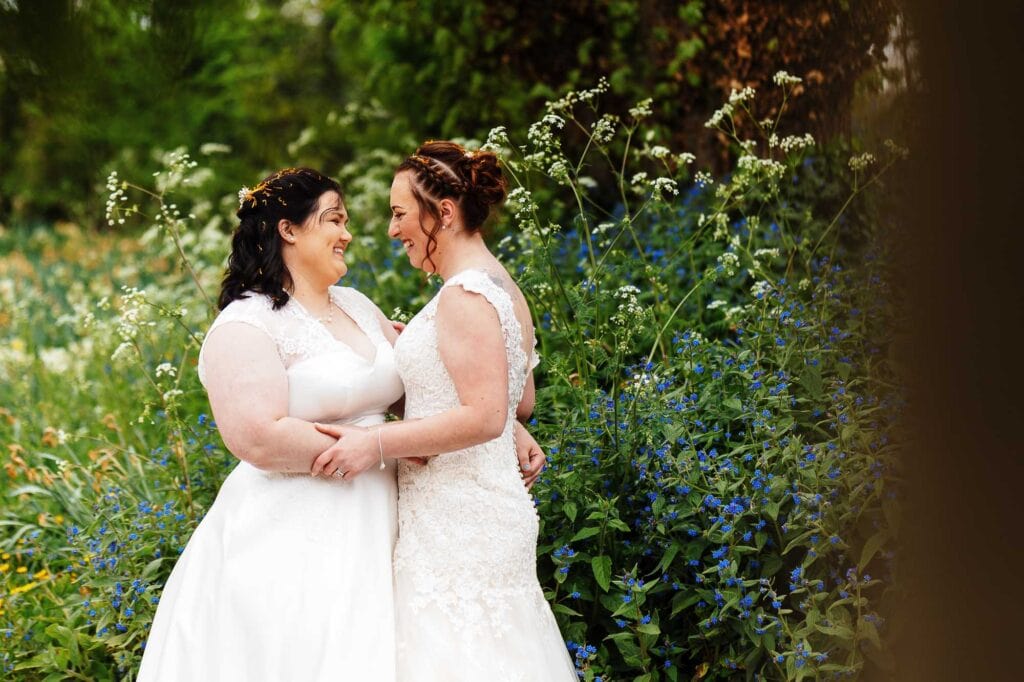 Elegant same-sex wedding couple smiling in a lush garden setting, captured by professional wedding photographer for BGS Weddings.