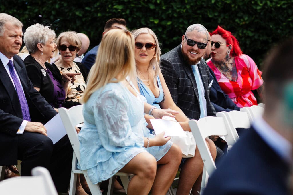 Elegant wedding guests seated outdoors at a garden ceremony, dressed in stylish attire, enjoying the special day with friends and family.