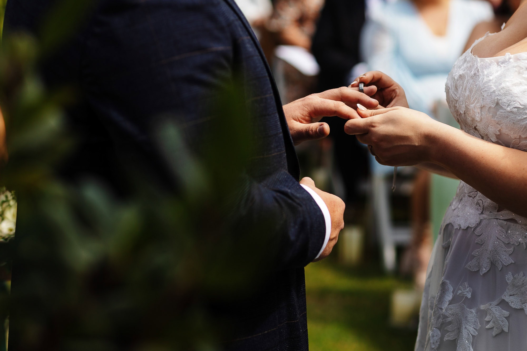 Delicate wedding vows exchange during an outdoor ceremony with a bride in a lace dress and groom in a dark suit, capturing a memorable moment for BGS Weddings.