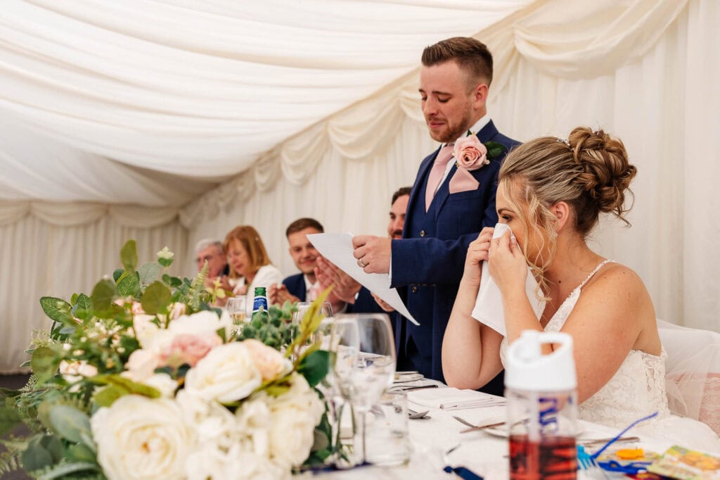Beautiful bride emotional during wedding speech at BGS Weddings, heartfelt moment captured in elegant wedding reception setting, showcasing romance and celebration.