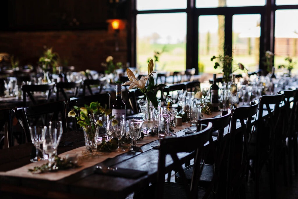 Elegant wedding reception setup with wooden tables, floral centrepieces, and glassware at BGS Weddings venue, perfect for a memorable celebration.