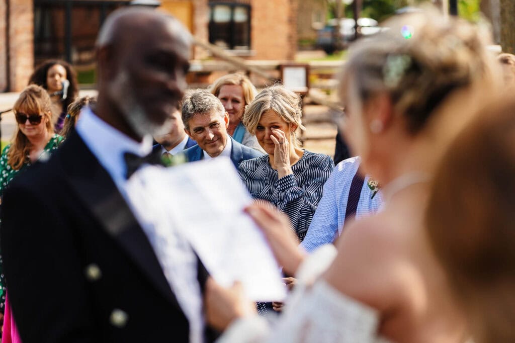 Elegant outdoor wedding ceremony featuring emotional vows with guests and family witnessing the special moment, set in a picturesque garden by BGS Weddings.