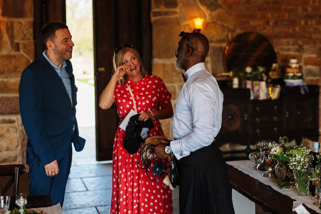 Photographs of guests at a wedding reception, engaging in lively conversation and laughter inside a rustic venue with exposed brick and wooden details.