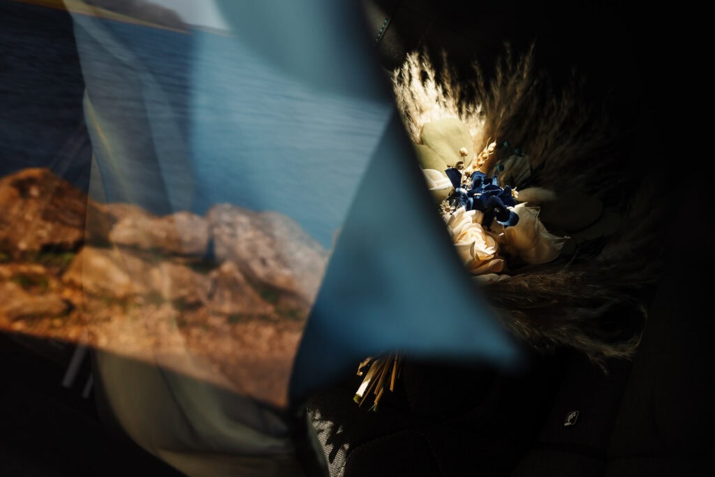 A close-up of a wedding bouquet featuring seashells, blue flowers, and natural elements, placed inside a car, highlighting a coastal or beach-themed wedding setting.