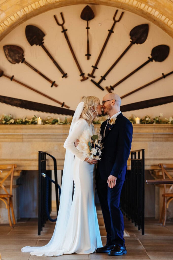 Wedding couple sharing a kiss at their ceremony in a historic venue with vintage tools decor.