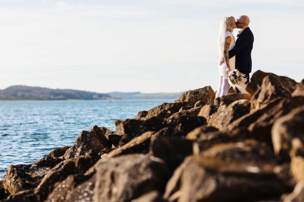 A romantic wedding scene featuring a bride and groom standing on rocks by the sea, capturing a special moment with a scenic coastal backdrop. Perfect for wedding photography and seaside wedding venues.