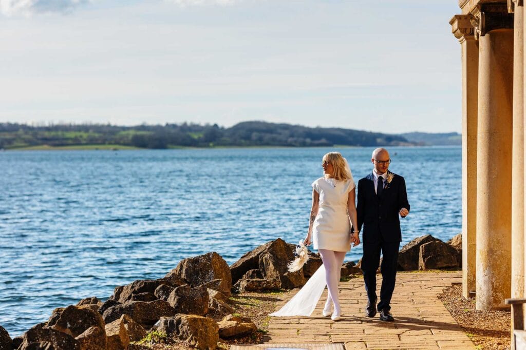 Wedding couple walking along the lakeside with scenic water and landscape background.