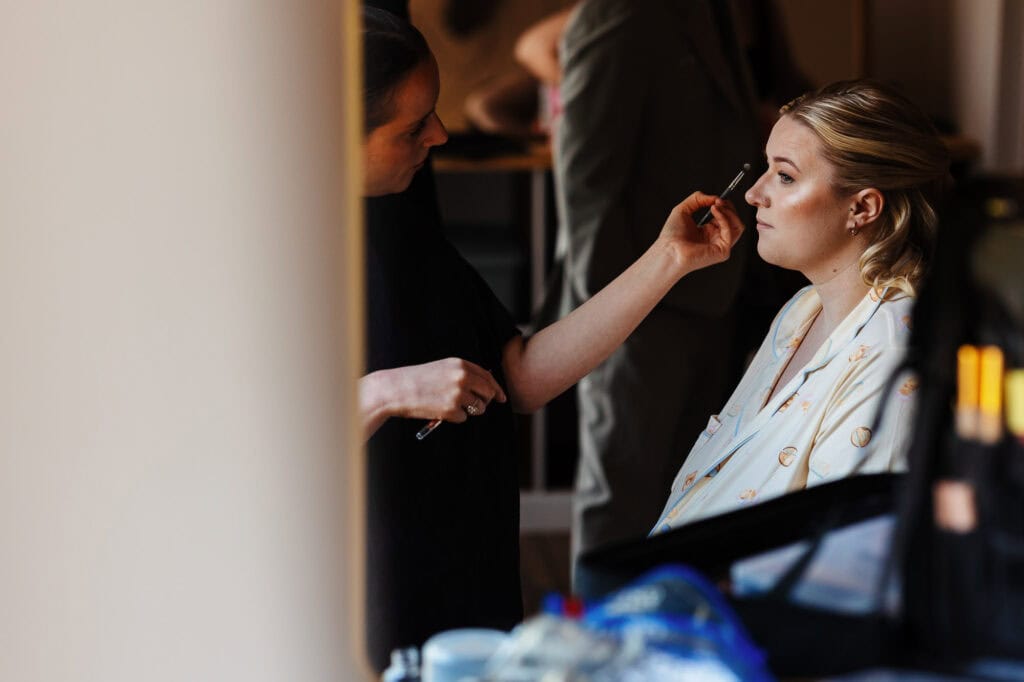 Bride getting her makeup done by a professional makeup artist before her wedding at BGS Weddings, showcasing expert bridal beauty services in a warm, elegant setting.