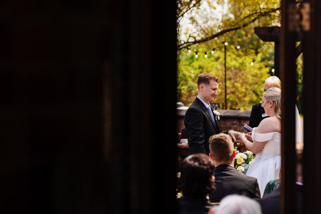 A1: Elegant outdoor wedding ceremony with bride and groom exchanging vows in a scenic garden setting, surrounded by guests and warm autumn lighting.