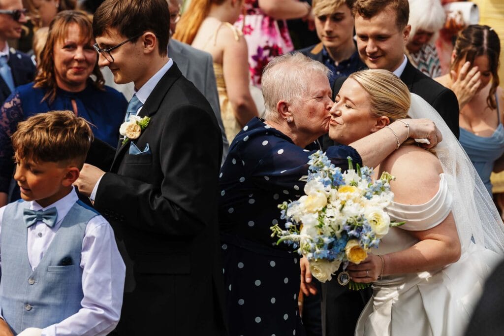 Heartwarming moment at a wedding as a bride embraces her elderly relative, surrounded by family and friends, celebrating love and family bonds.