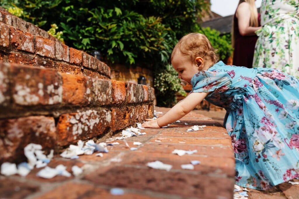 A woman and a young girl cleaning up scattered paper on a brick pathway during an outdoor wedding event.