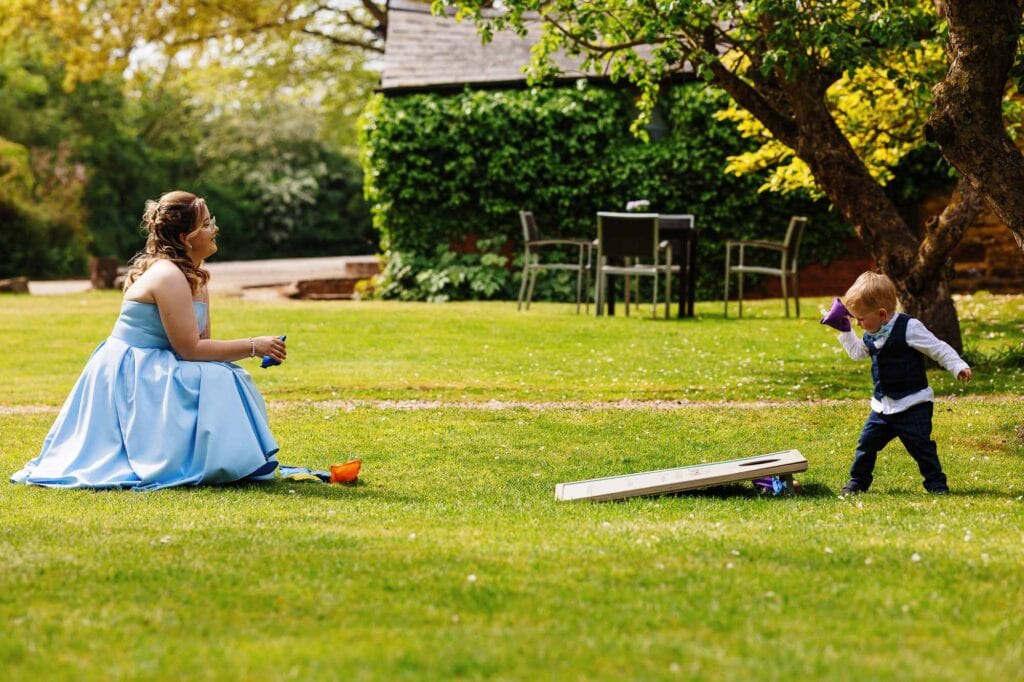 A woman in a blue dress playing with a young boy outdoors on a grassy lawn during daytime, with trees and garden furniture in the background.