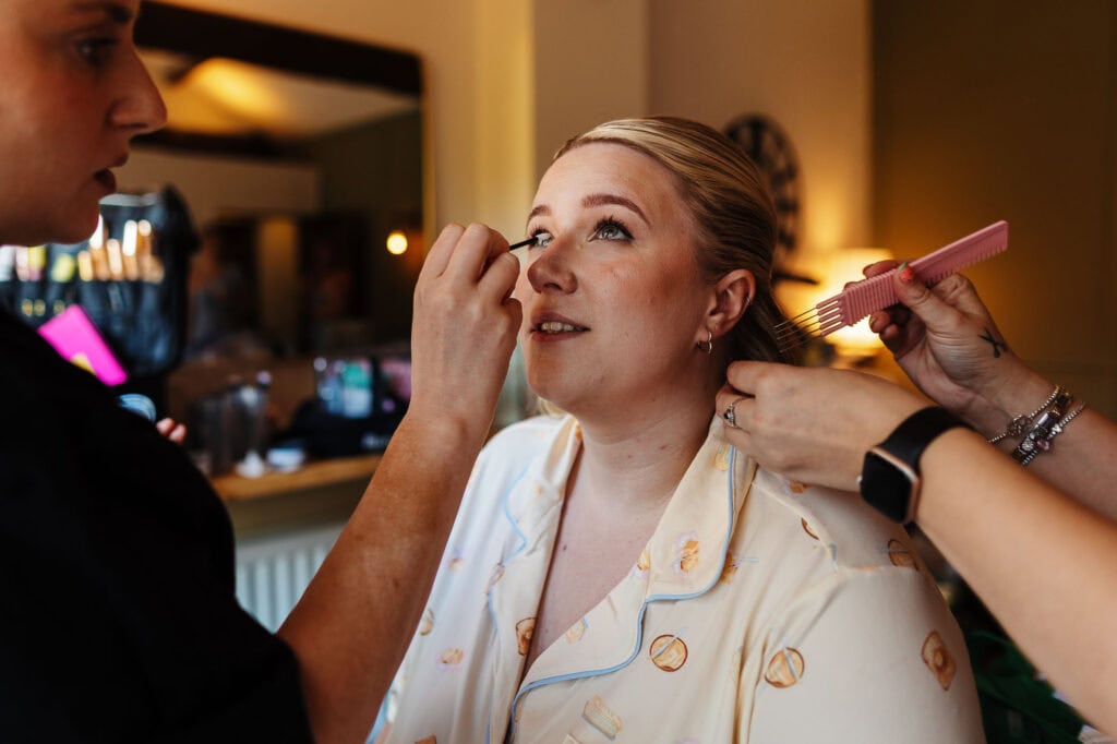 Professional makeup artist applying makeup to a bride in a warmly lit room, preparing for her wedding day, showcasing expert beauty services for special occasions.