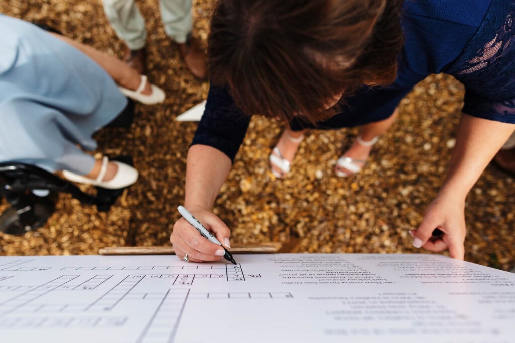 A detailed wedding planning consultation with a bride reviewing her wedding layout on a large paper, surrounded by fallen leaves, showcasing outdoor wedding preparations.