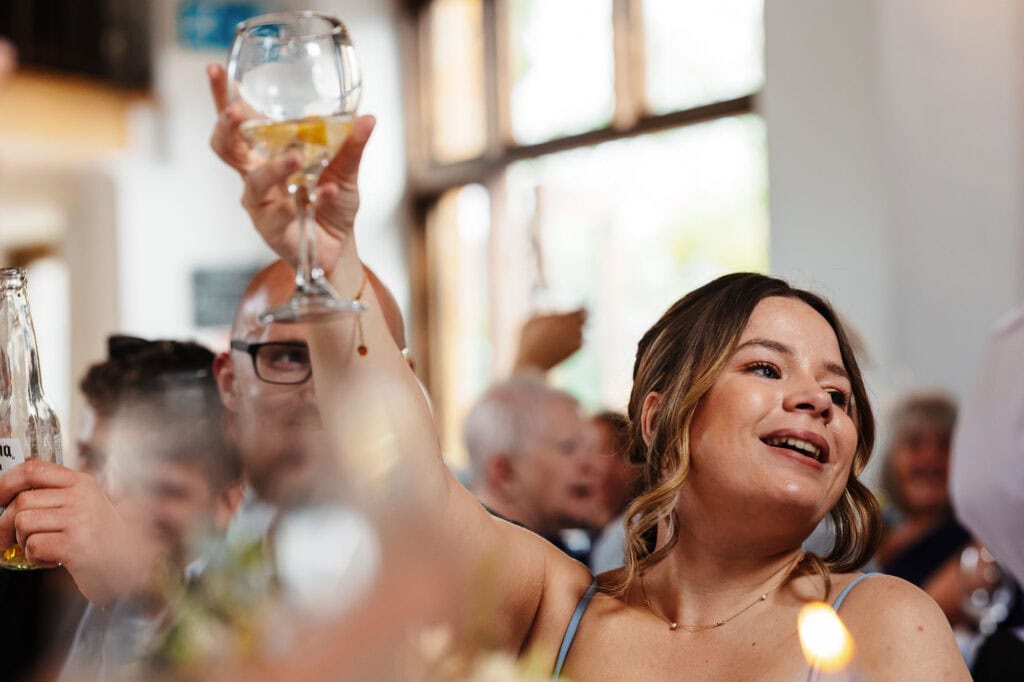 Celebrating a wedding toast with a woman raising a glass, surrounded by joyful guests in a bright, elegant venue, capturing happiness and festive atmosphere.